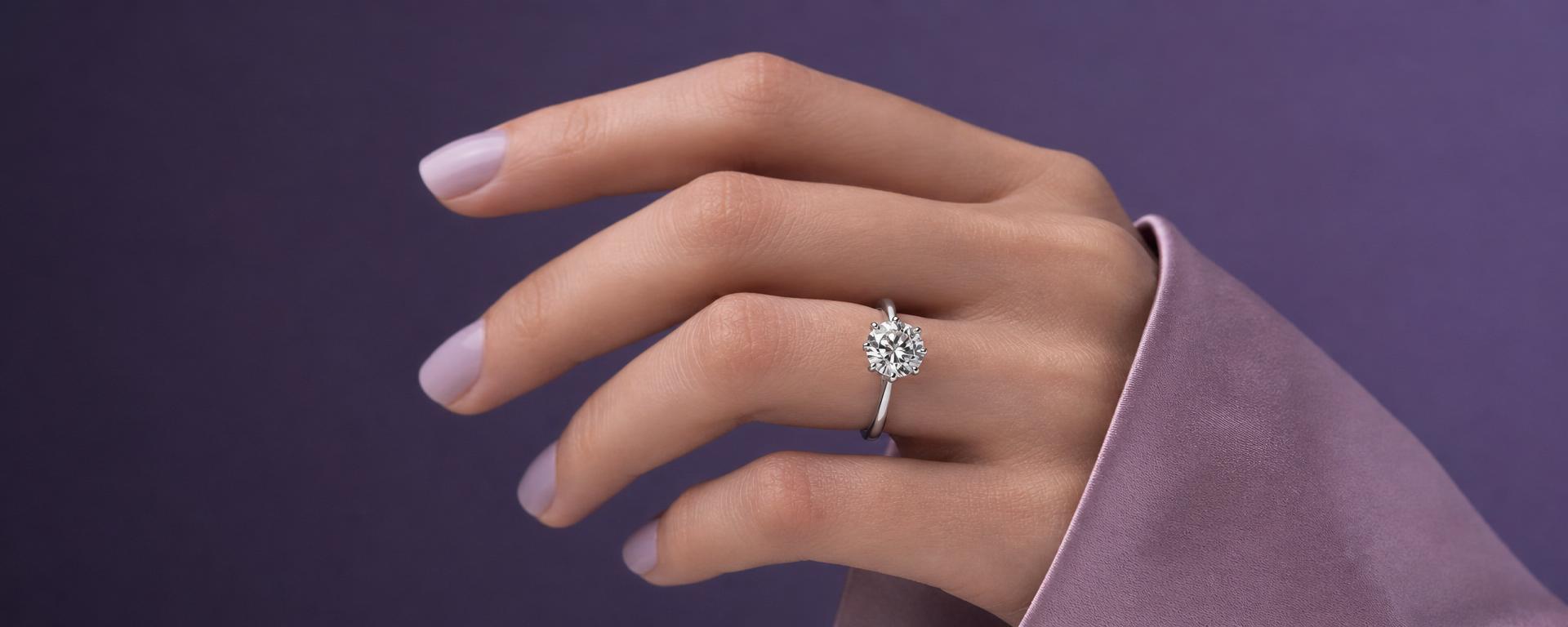 Elegant hand wearing a luxury diamond solitaire ring against a violet background